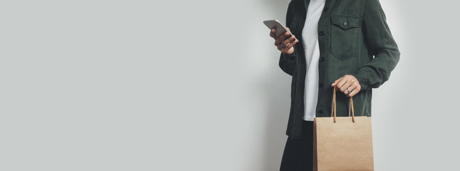 Person mit Einkaufstüte, die auf ihr Smartphone schaut.