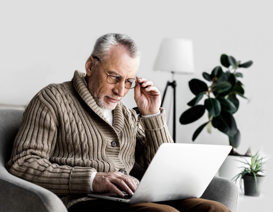 Sehbeeinträchtigter Mann schaut durch seine Brille auf Notebook.