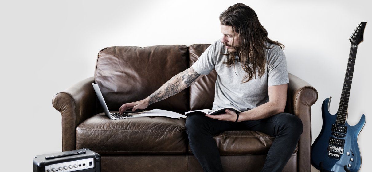 Musiker arbeitet am Sofa sitzend an seinem Notebook mit der Erweiterung digitale Güter.