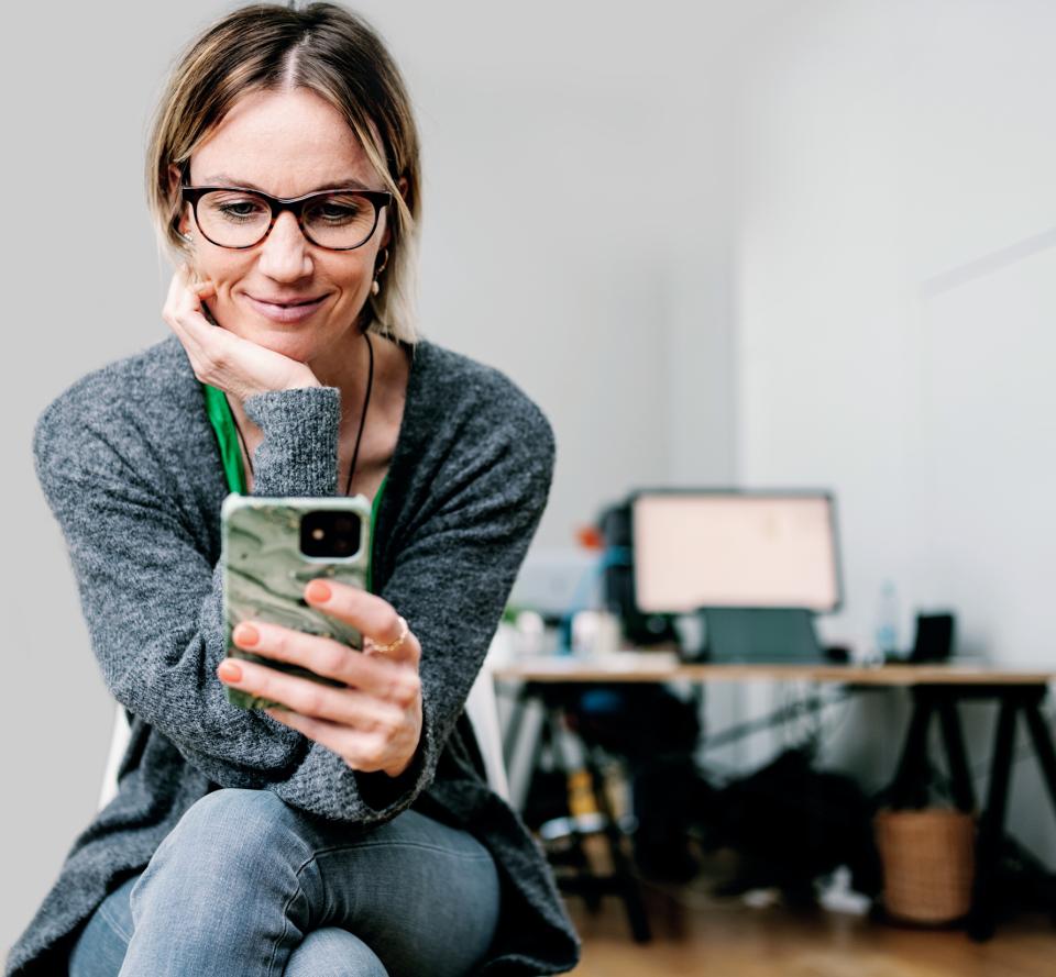 Frau schaut auf ihr Handy und betrachtet einen Newsletter.